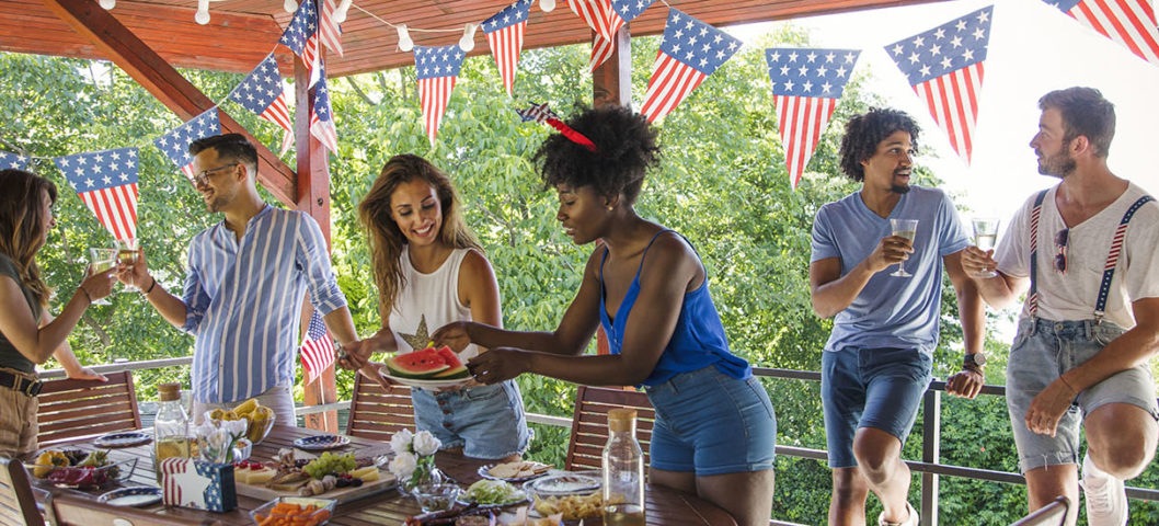 Group-of-friends-celebrating-a-summer-party-with-outdoor-home-decor-and-fourth-of-July-banners