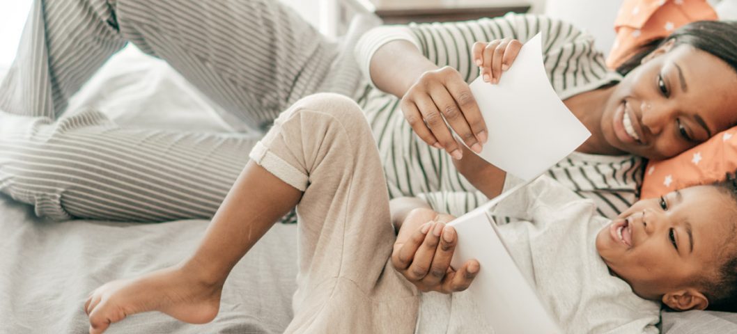 Mom and daughter reading book on bed together