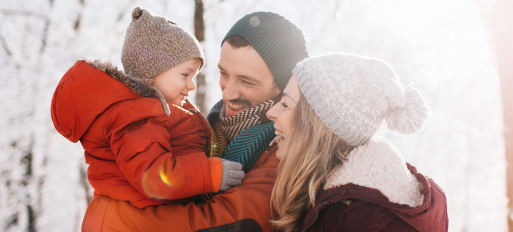 A mom, dad, and young child in the snow for holiday card photos