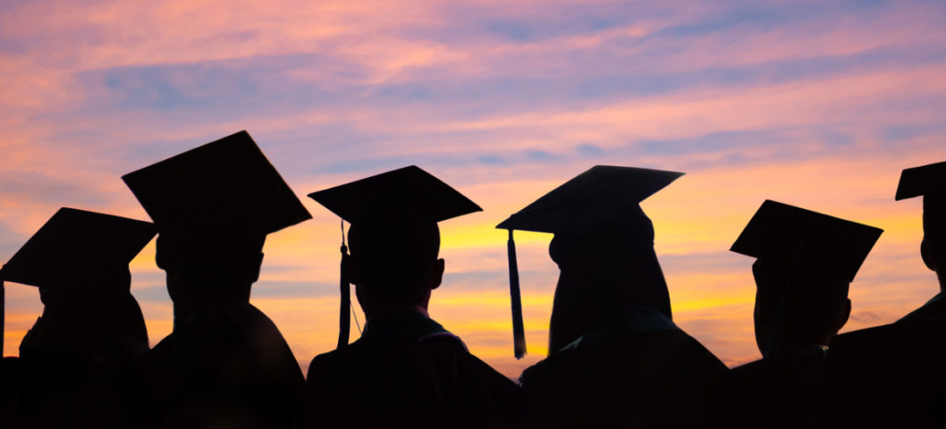 A group of students with their caos and gowns on in the sunset on graduation day