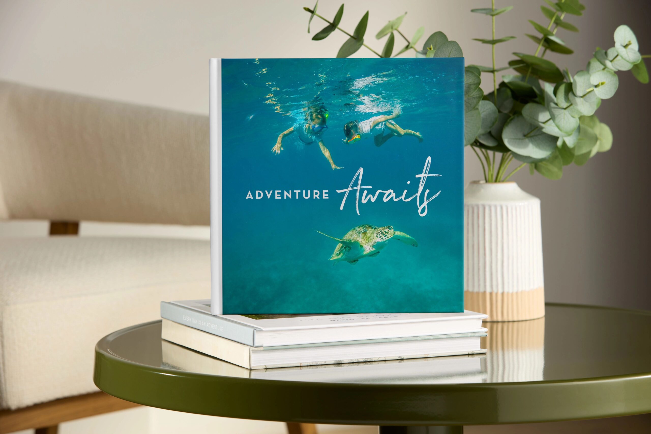 Travel photo book that says Adventure Awaits on the cover with pictures of kids swimming in the ocean with fish