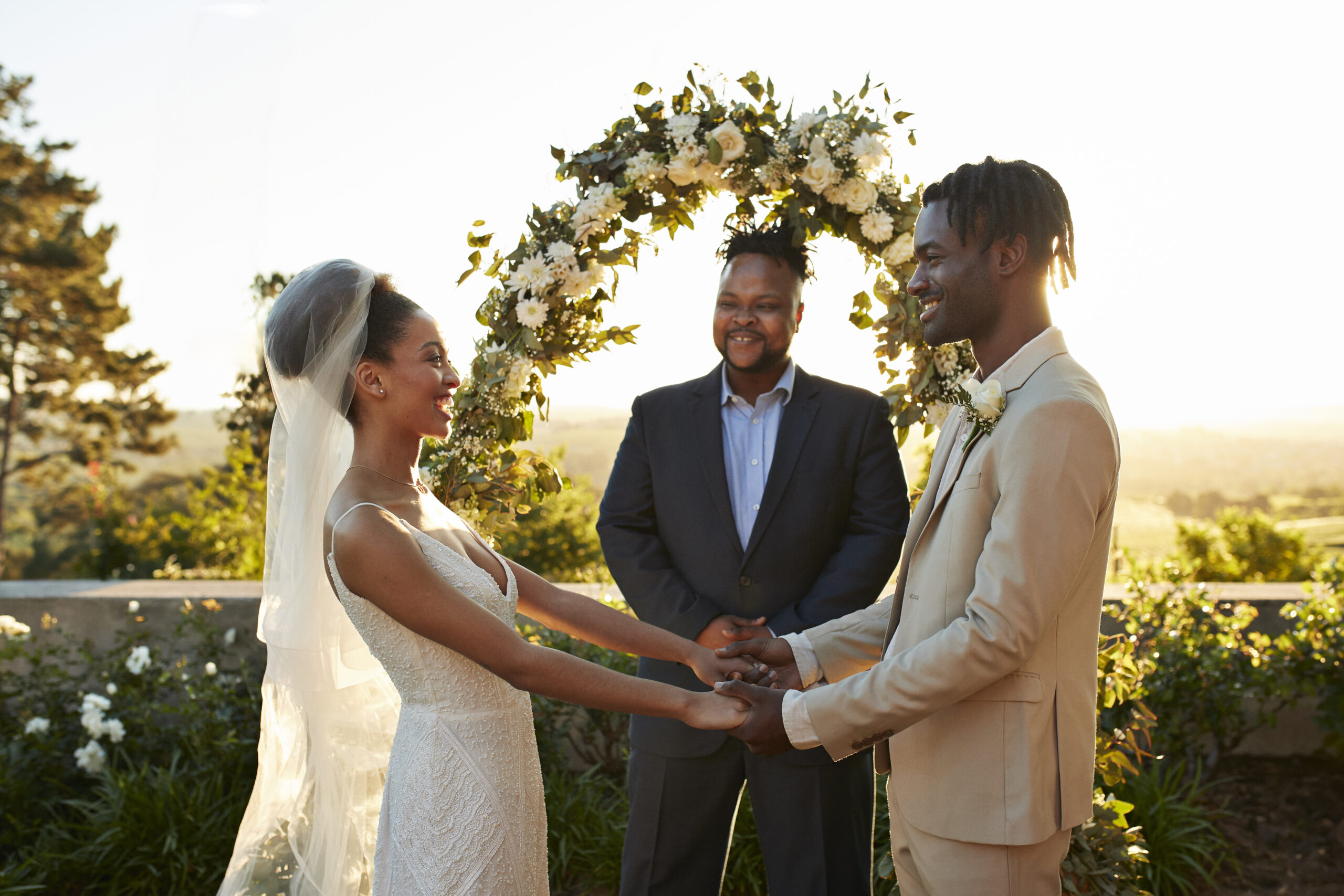 Happy young couple holding hands standing by minister at wedding altar during ceremony