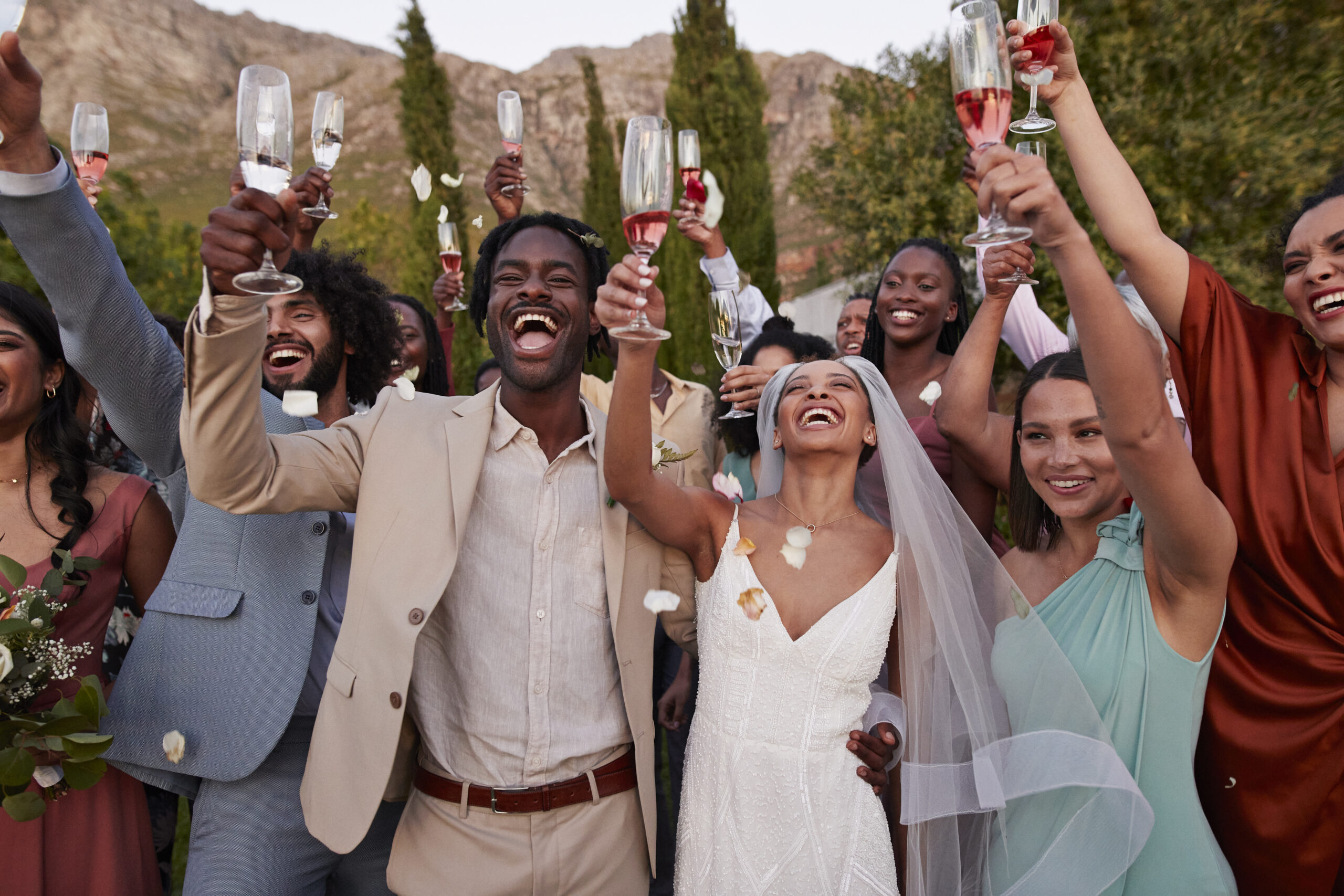 Confetti falling on happy just married couple and wedding guests with drinks standing at reception during sunset